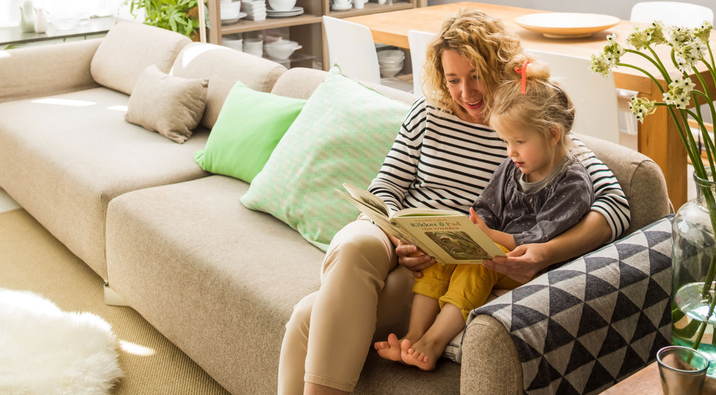 Vrouw en dochter knus op de bank met voorleesboek.