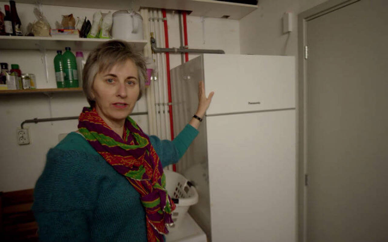 Vrouw staat bij warmtepomp in bijkeuken. Het apparaat lijkt op een grote koelkast.