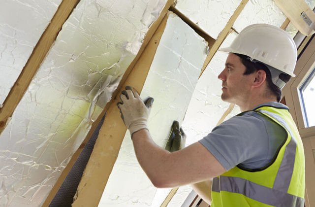 Man met helm en handschoenen brengt dakisolatie aan.