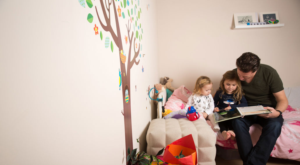 Vader leest kinderen voor op bed. Een duurzaam huis is energiezuinig en comfortabel.