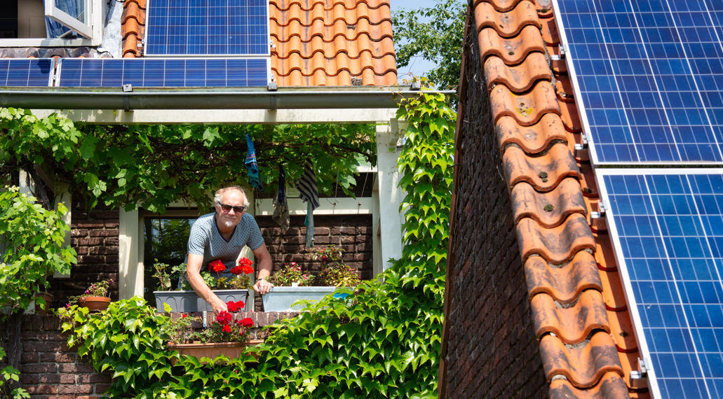 Man kijkt uit raam, op het dak liggen zonnepanelen. Wek zelf duurzame stroom op.