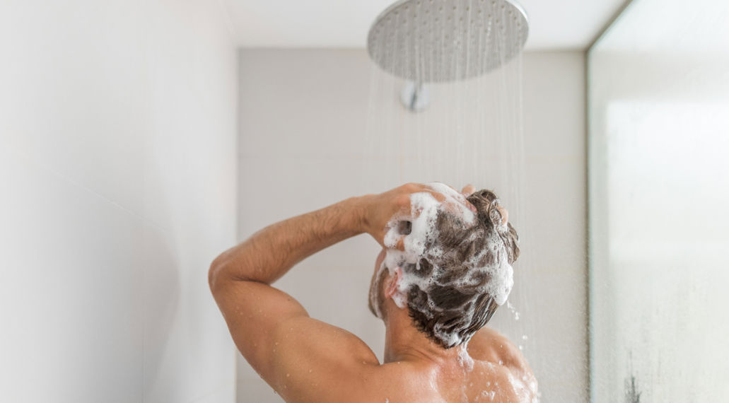 Man onder de douche met shampoo in haar.
