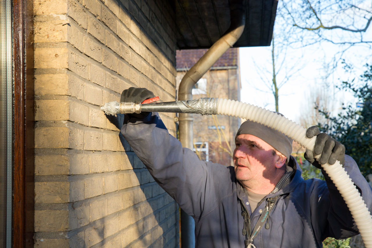 Medewerker isolatiebedrijf spuit met een grote slang isolatiemateriaal in de spouwmuur.
