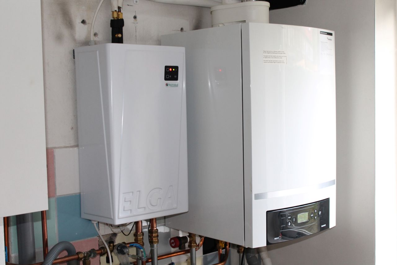 Foto van een cv-ruimte, met een hybride warmtepomp naast een cv-ketel.