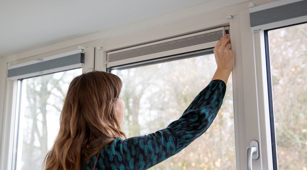 Een vrouw doet het ventilatierooster in haar raam open.