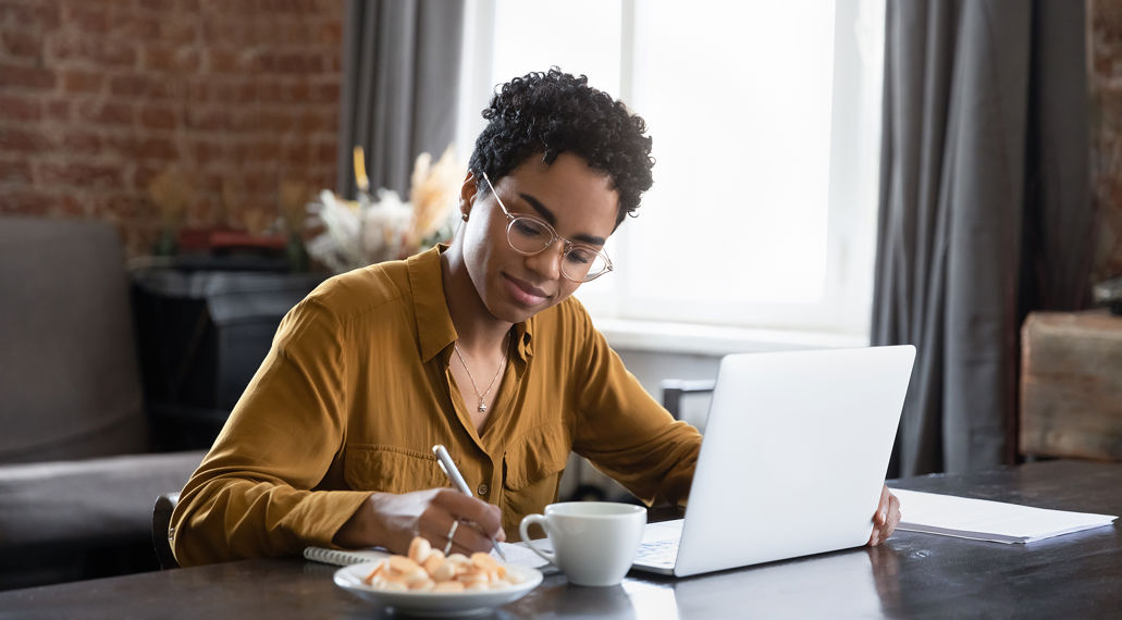 Vrouw aan tafel met laptop schrijft iets op