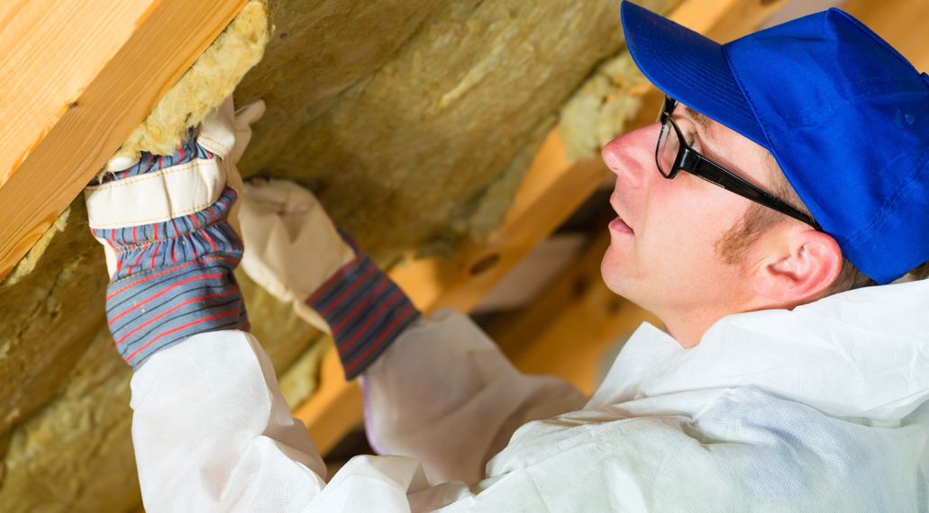 Een man met een blauwe pet en beschermende kleding isoleert een schuin dak met glaswol.