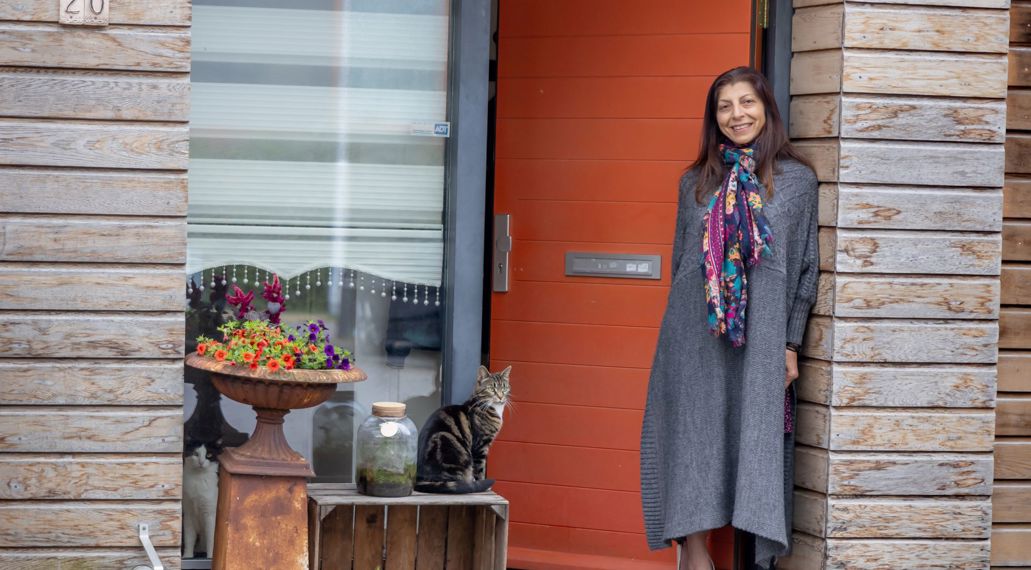Een vrouw staat lachend bij de voordeur van haar huurhuis.
