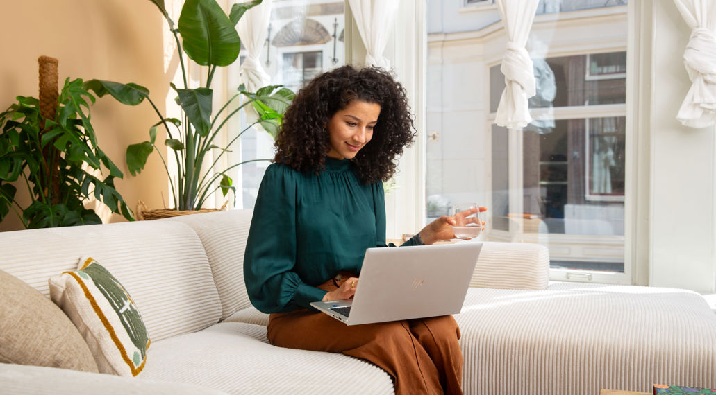 Een vrouw zit met haar laptop op de bank.