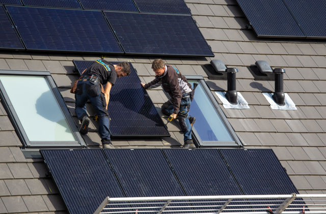 Twee mannen plaatsen zonnepanelen op het dak van een huis.