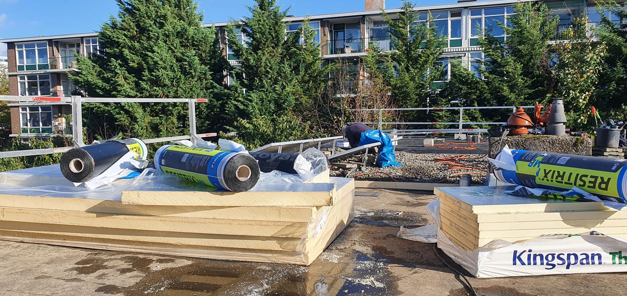 Foto van een isolatie-expert aan het werk op een plat dak. Om hem heen liggen isolatiematerialen.,