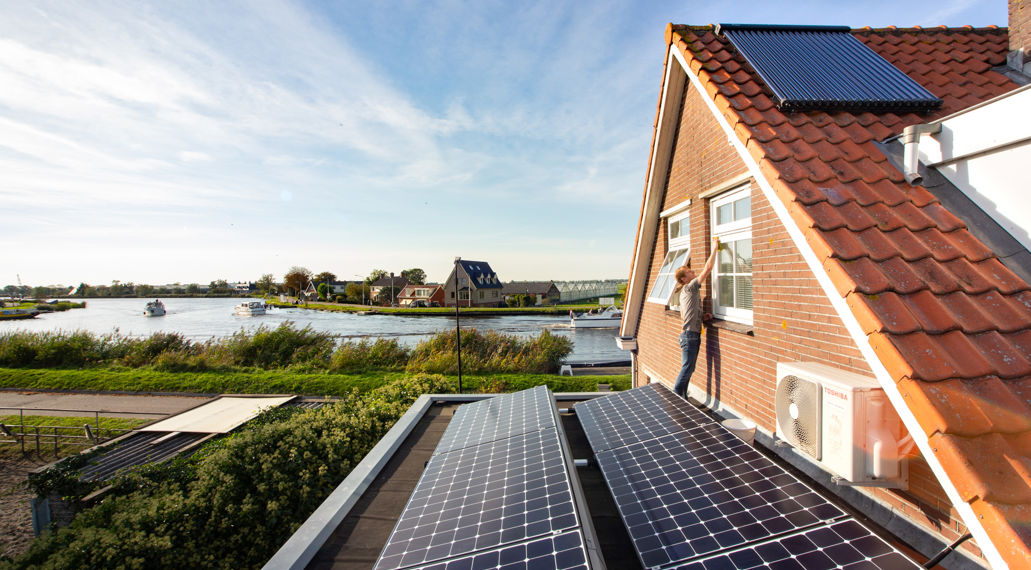 Man op dak met zonnepanelen en zonneboiler.