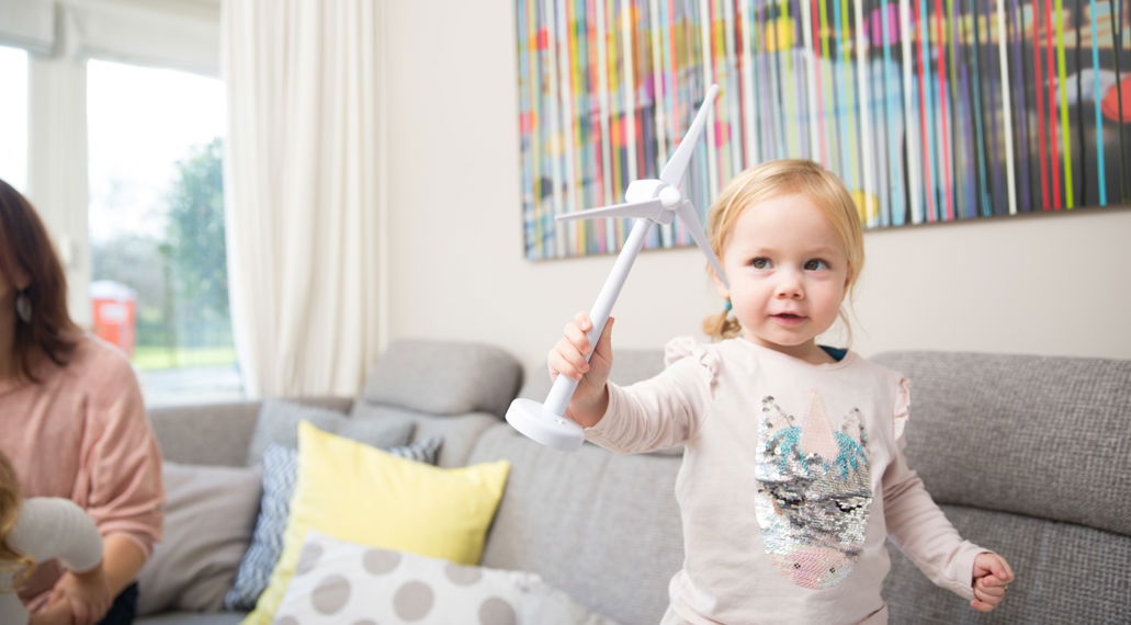 Meisje met speelgoed windmolentje op de bank. Bespaar energie door je huis te verduurzamen.
