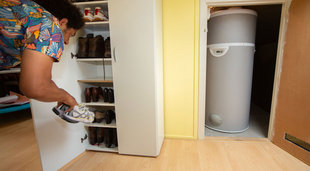 Man bij schoenenkast naast warmtepomp op zolder.