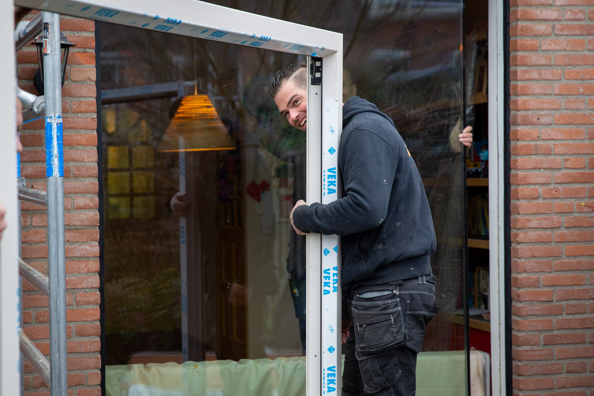 Op de afbeelding zie je een man voor een buitenmuur die een kozijn met triple-glas tilt.