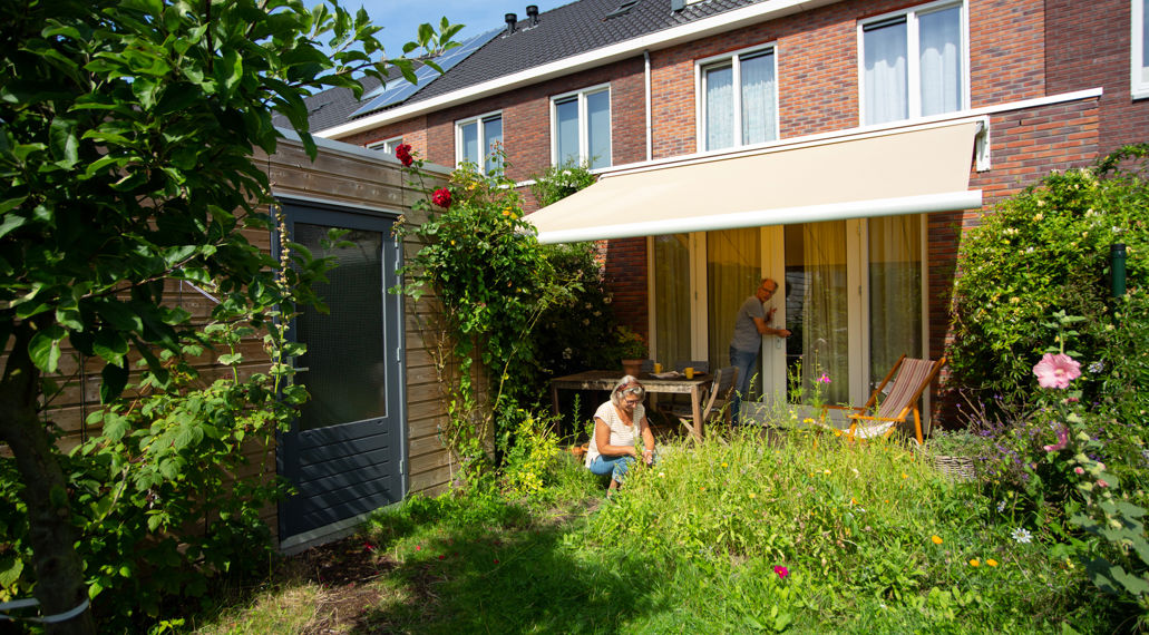 Huis met zonnescherm, vrouw is bezig in de tuin.