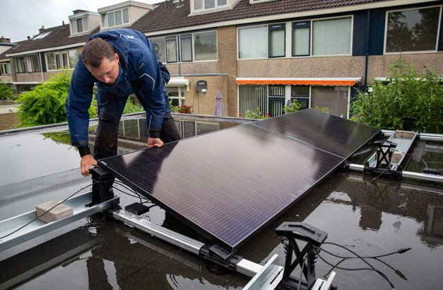 Een installateur plaatst zonnepanelen op een plat schuurdak.