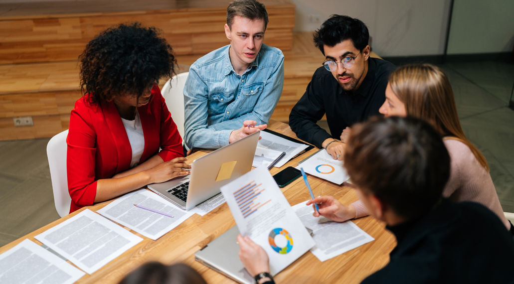 Groep jonge mensen aan tafel met laptop en papieren. Samenwerken en overleg.