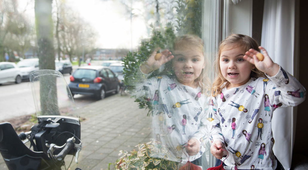 Meisje staat bij het raam en zwaait. Met isolatieglas is het lekker warm in huis en bespaar je energie.
