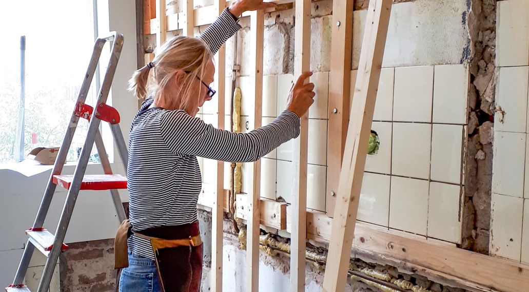 Vrouw schroeft latten tegen de muur voor voorzetwand.