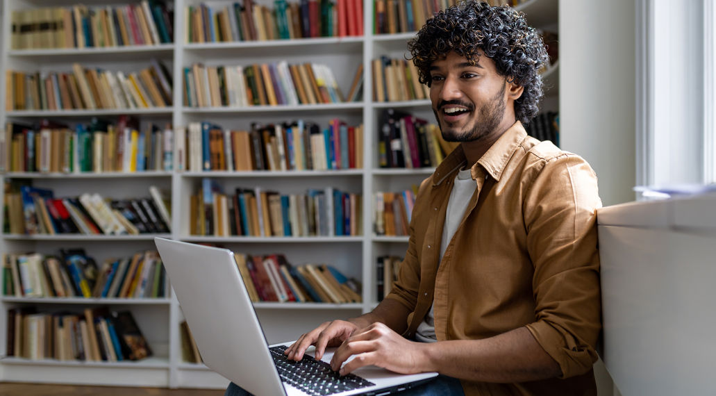 Man met laptop voor boekenkast vol boeken