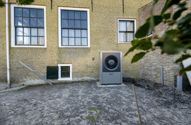 Buitenunit van een hybride warmtepomp tegen de muur van een monumentaal pand.