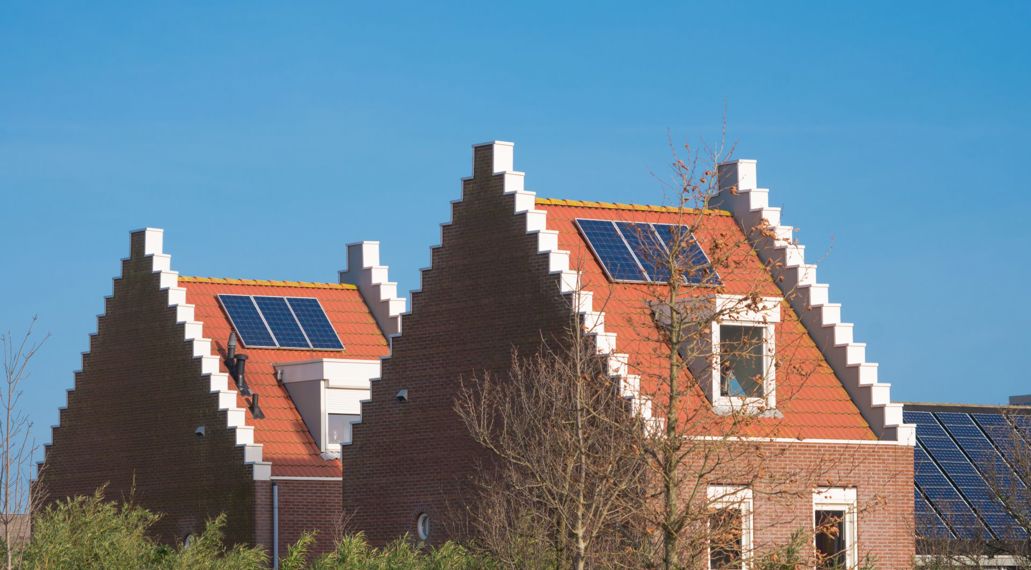 Op de foto staan twee woningen met een trapgevel schuin achter elkaar. Op het dak van de woningen liggen zonnepanelen.