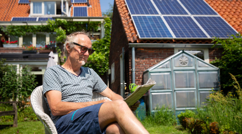 Man in tuin, huis met zonnepanelen op de achtergrond.